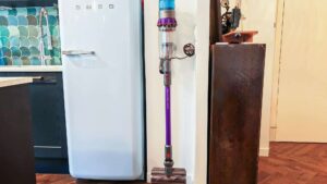 Aspirateur balai Dyson Gen5 Detect rangé sur son support mural, entre un réfrigérateur et un meuble, dans une cuisine