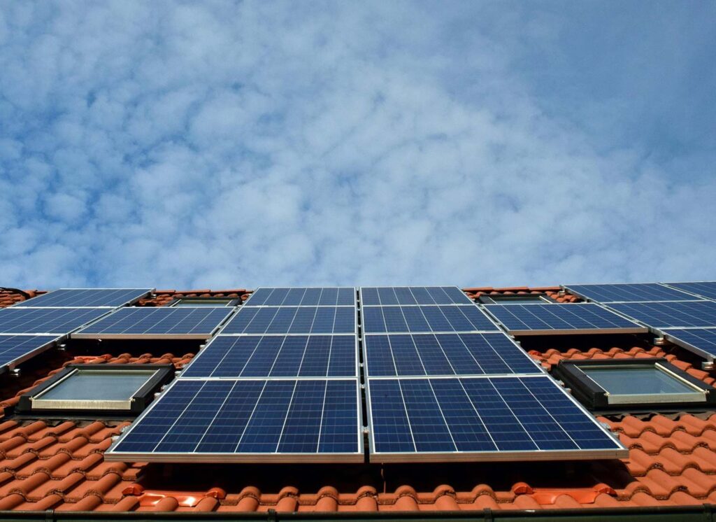 Panneaux solaires posés sur une toiture en tuiles rouges, sous un ciel bleu partiellement nuageux
