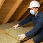 Ouvrier posant de l’isolant dans un grenier sous toiture en bois