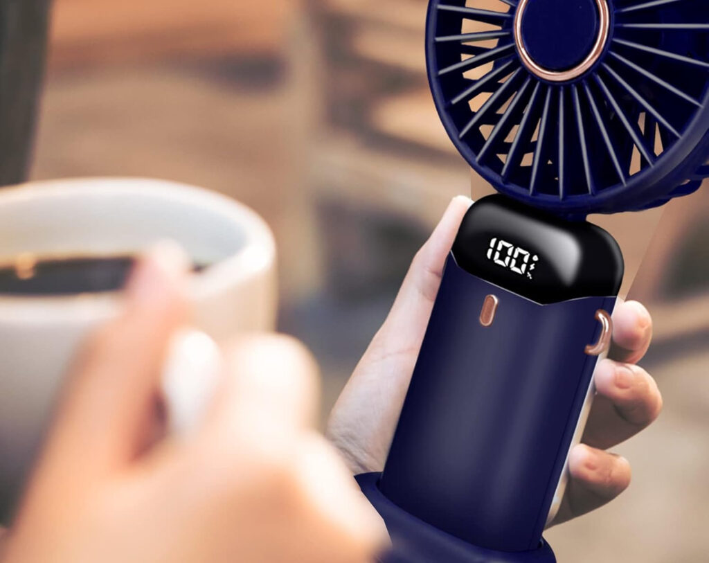 Personne en terrasse prenant un café tout en se ventilant avec un mini ventilateur portable