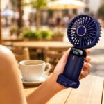 Personne utilisant un mini ventilateur portable en terrasse pendant une journée de forte chaleur