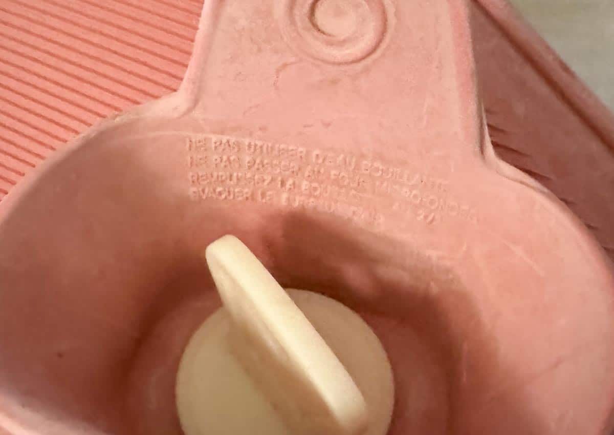 Gros plan sur le bouchon d’une bouillotte indiquant les règles de sécurité à suivre pour éviter tout risque d’éclatement ou de brûlure