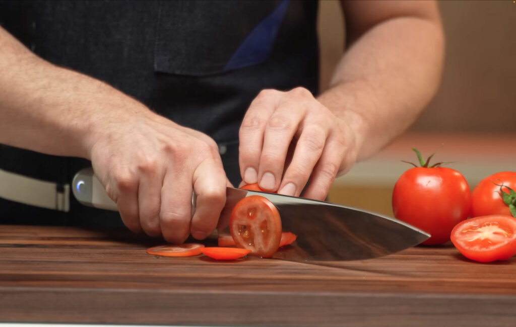 Couteau ultrasonique C-200 en train de trancher une tomate sur une planche à découper.