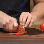 Couteau ultrasonique C-200 en train de trancher une tomate sur une planche à découper.