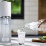 Machine SodaStream Gaia sur un plan de travail avec un verre d’eau pétillante