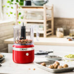 Mini hachoir sans fil KitchenAid 5KFCB519EER rouge avec bol de 1,2 L sur un plan de travail