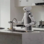 Robot domestique SwitchBot Onero H1 utilisant ses bras articulés pour manipuler des objets sur un plan de travail, comme des tasses ou du linge.