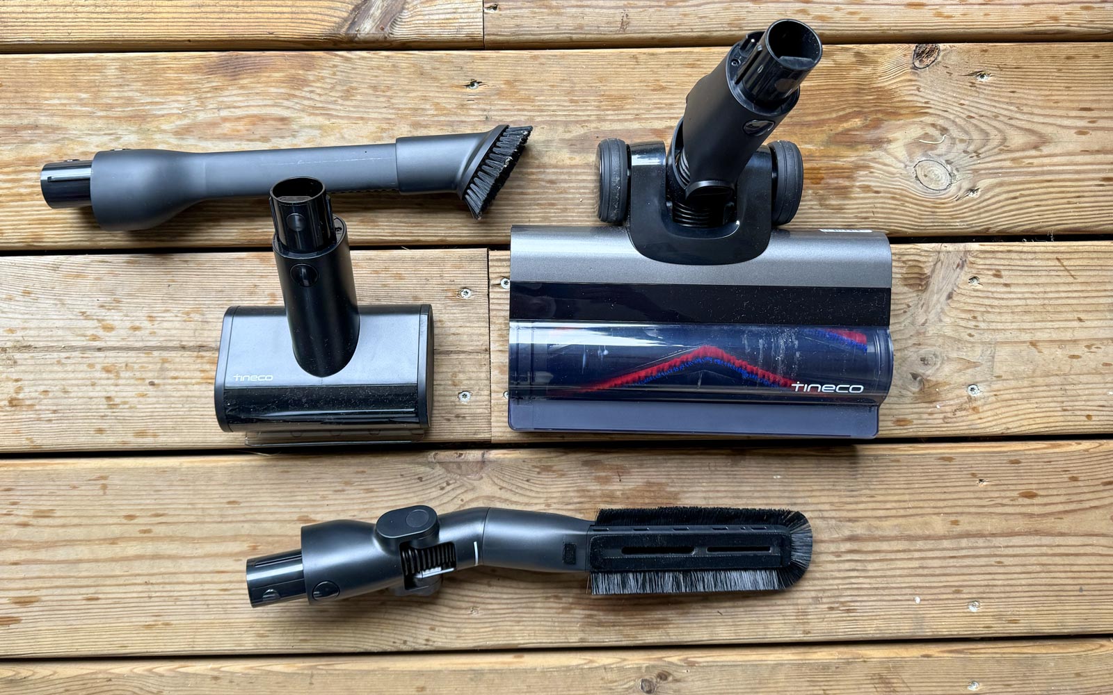 Vue d'ensemble à plat des accessoires de l'aspirateur Tineco Pure One A90S : brosse principale avec LED, mini turbo-brosse, suceur long pour fentes et brosse douce pour meubles, disposés sur un sol.