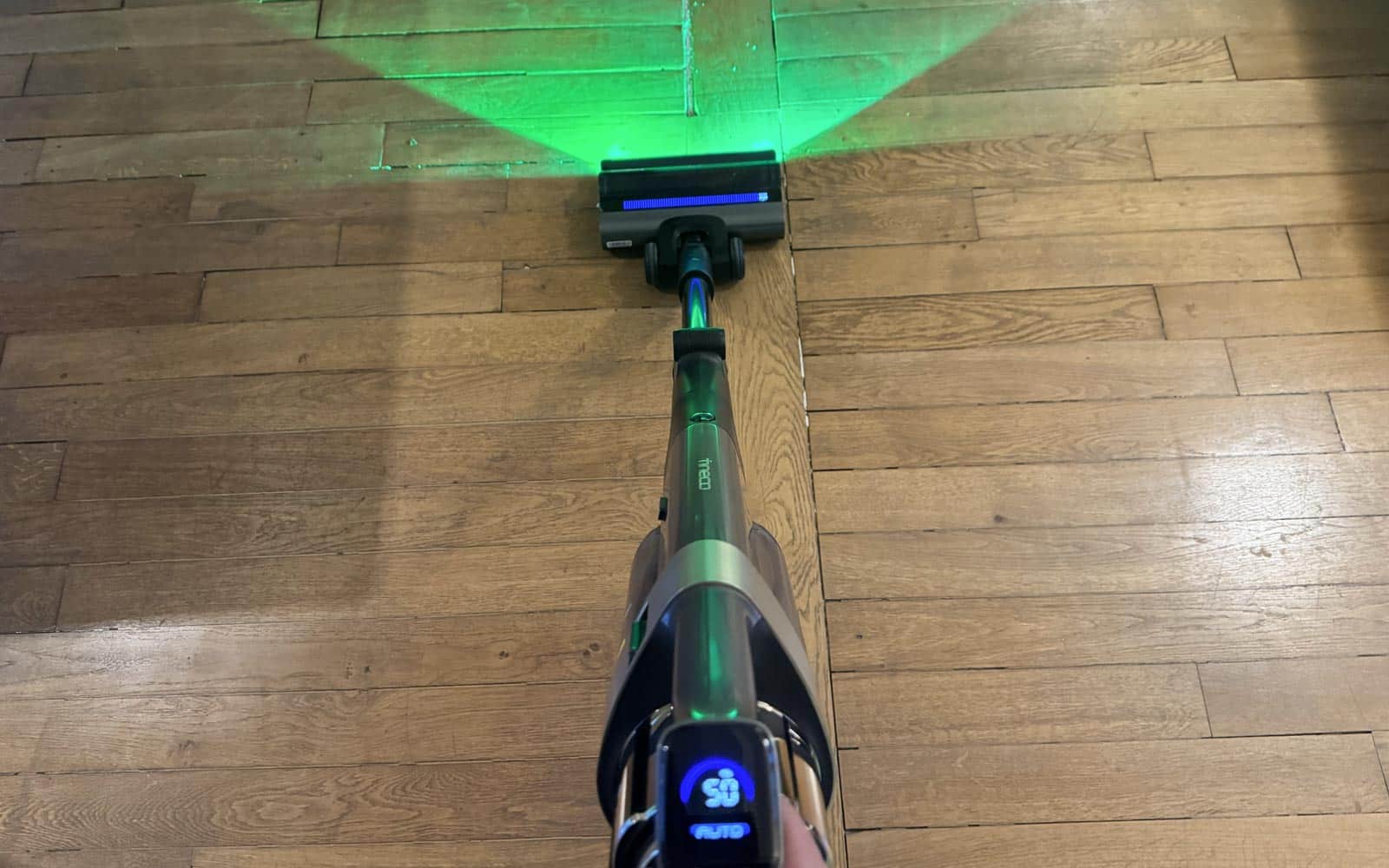 Aspirateur Tineco A90S aspirant entre les lattes d'un parquet en bois ancien.