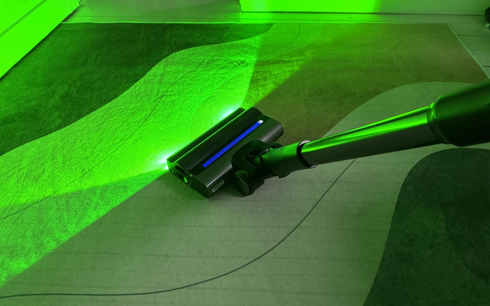 Aspirateur balai Tineco A90S avec éclairage vert sur un tapis à motifs.