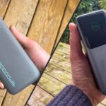 Comparaison côte à côte de deux batteries externes de 20 000 mAh : la Ugreen Nexode Pro 130W à droite, de forme colonne avec un grand écran TFT, et la Cuktech PB200N à gauche, plus fine avec son câble USB-C intégré faisant office de dragonne.
