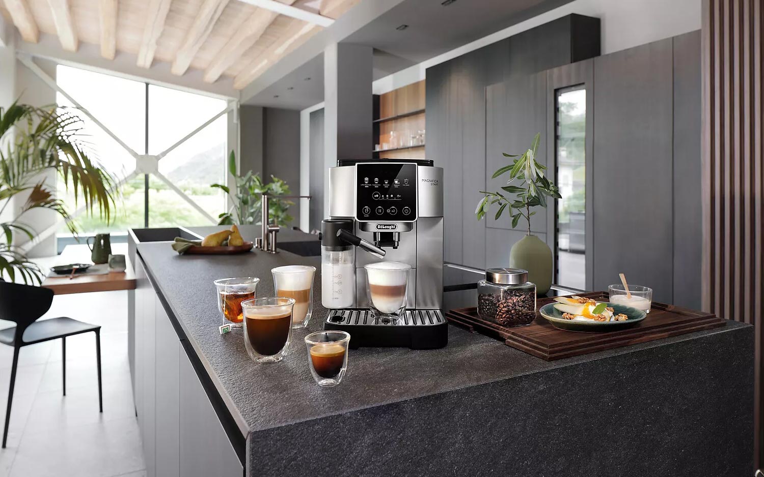Une machine à café expresso automatique Delonghi Magnifica Start avec une carafe à lait latérale, préparant un cappuccino dans une tasse en verre, posée sur un plan de travail de cuisine