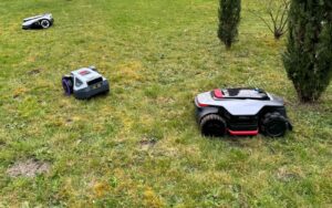 Trois robots tondeuses sans fil (Dreame A3 AWD Pro 5000, Ecovacs GOAT A1600 LiDAR PRO et Anthbot M9) alignés sur une pelouse lors d'un test comparatif.