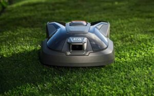 Robot tondeuse Husqvarna Automower sur une pelouse verte, illustrant l'offre d'extension de garantie de 5 ans et la technologie de navigation par vision IA sans câble périphérique.