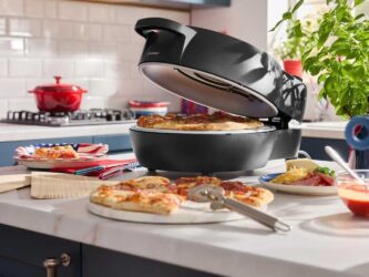 Four à pizza électrique Silvercrest de Lidl ouvert avec une pizza sur la pierre réfractaire et des parts sur un comptoir de cuisine.