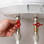 Robinets d'arrêt rouges sous un chauffe-eau électrique blanc, manipulation des vannes d'eau chaude
