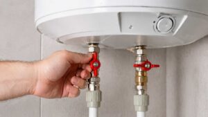 Robinets d'arrêt rouges sous un chauffe-eau électrique blanc, manipulation des vannes d'eau chaude