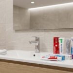 Plusieurs dentifrices blancheur et une brosse à dents posés près d’un lavabo dans une salle de bain moderne