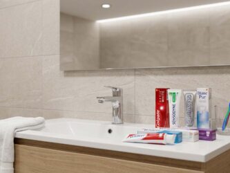 Plusieurs dentifrices blancheur et une brosse à dents posés près d’un lavabo dans une salle de bain moderne