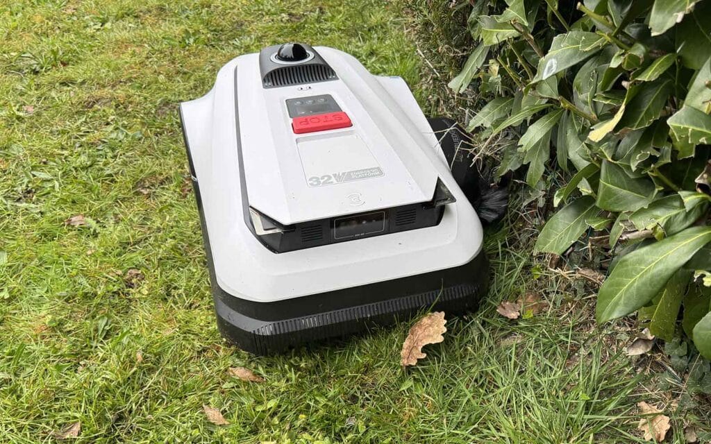 Robot tondeuse Ecovacs Goat A1600 LiDAR PRO coupant l'herbe le long d'une haie.