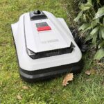 Robot tondeuse Ecovacs Goat A1600 LiDAR PRO coupant l'herbe le long d'une haie.