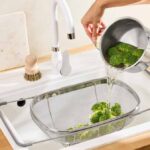 Passoire d'évier Lidl en acier inoxydable positionnée au-dessus du bac pour égoutter des brocolis.
