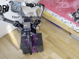 Photo du robot open source YOR dans une chambre à coucher. Le robot utilise ses deux bras articulés mettre du linge dans un panier à linge au sol à côté de lui.