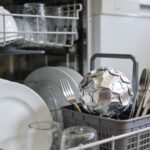 Lave-vaisselle ouvert avec vaisselle propre et une boule d'aluminium froissée dans le panier à couverts