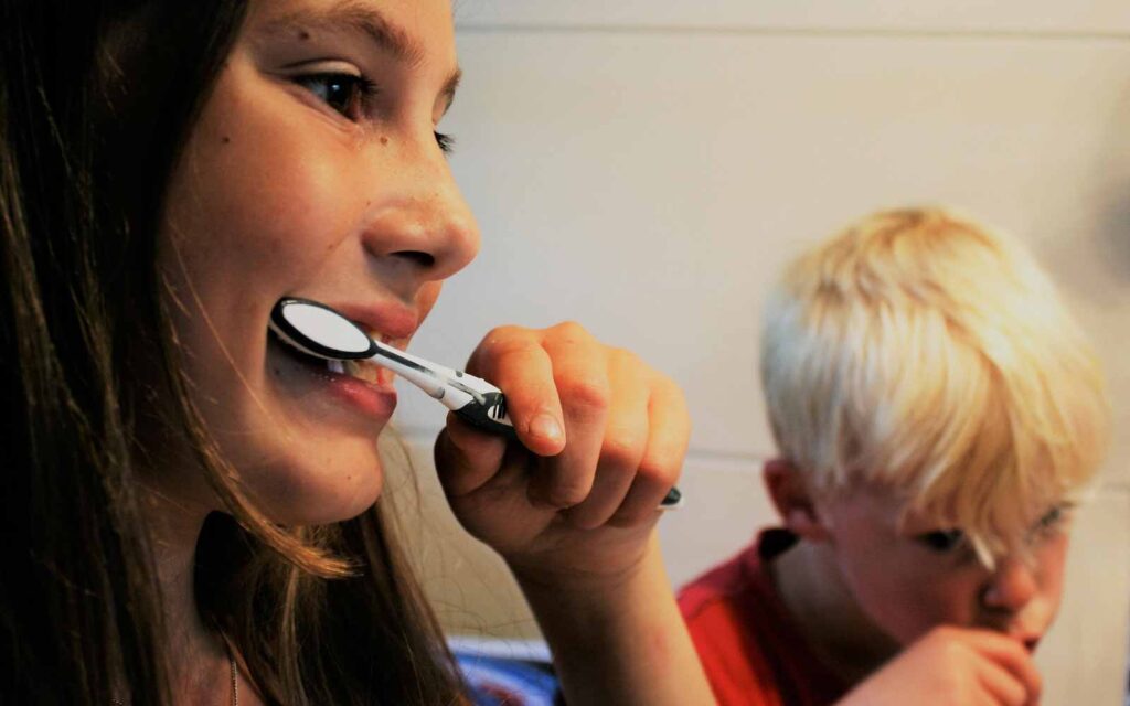 Deux personnes se brossant les dents avec un dentifrice fluoré devant le miroir de la salle de bain