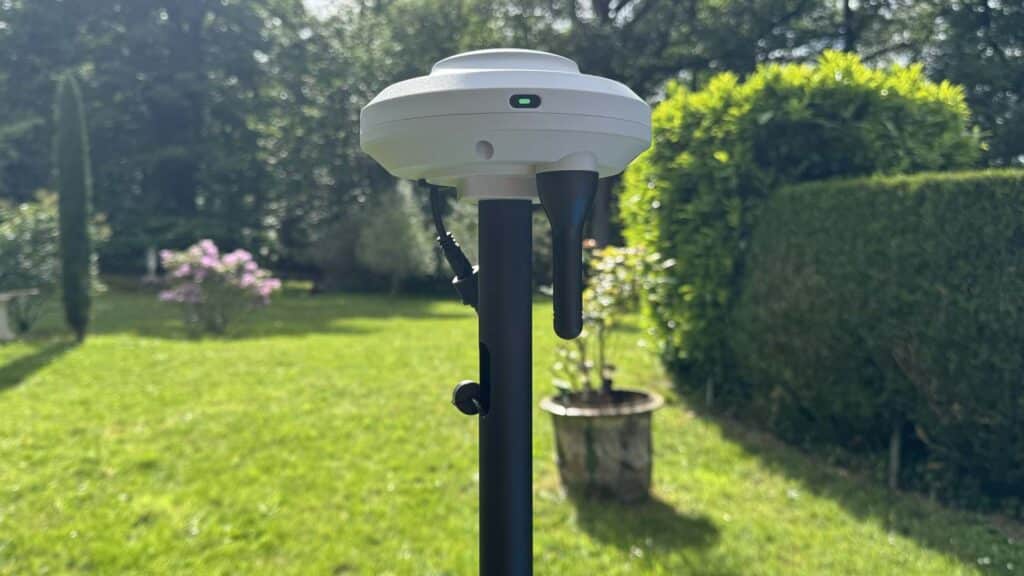 Balise RTK de robot tondeuse installée dans le jardin avec voyant vert indiquant une bonne réception du signal GPS