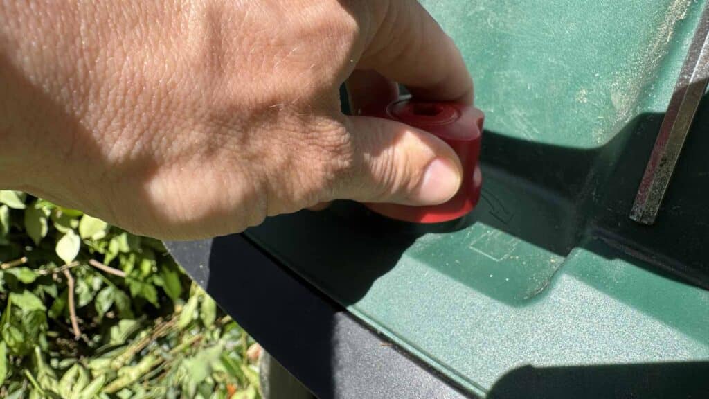 Main dévissant la molette rouge de verrouillage du broyeur de végétaux Parkside pour ouvrir le capot.