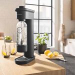 Machine à soda Grohe Blue Fizz Premium en train de gazéifier une bouteille d'eau sur un plan de travail de cuisine.