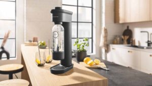 Machine à soda Grohe Blue Fizz Premium en train de gazéifier une bouteille d'eau sur un plan de travail de cuisine.