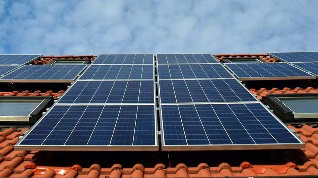 Panneaux solaires posés sur une toiture en tuiles rouges, sous un ciel bleu partiellement nuageux