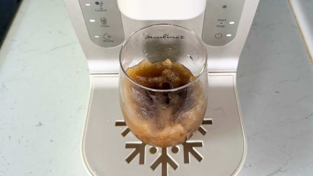 Gros plan sur la texture d'un slushy au Coca-Cola dans un verre posé sur le repose-gouttes de la Moulinex Freezi.
