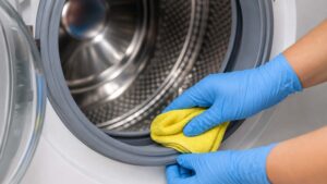 Personne nettoyant le joint d’une machine à laver à hublot avec un chiffon microfibre jaune