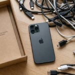 Boîte de smartphone vide entourée de plusieurs câbles USB-C différents, illustration de la confusion autour des normes de charge et de transfert.