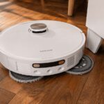 Le robot aspirateur laveur Dreame L40 Ultra AE nettoie un parquet au plus près d’un meuble