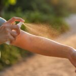 Personne appliquant un spray anti-moustique sur son bras en extérieur