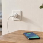 Chargeur de smartphone branché à une prise murale dans un salon, avec téléphone posé sur une table en bois.