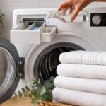 Serviettes blanches pliées devant un lave-linge ouvert, avec du vinaigre blanc versé dans le bac à produits.