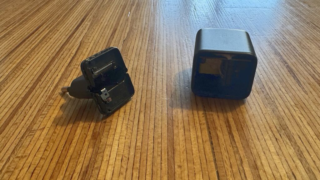 Les deux morceaux d’un chargeur USB-C cassé posés sur une table en bois : la partie fiche avec ses broches et le boîtier vide