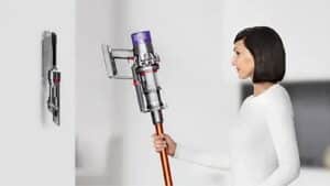 Femme tenant un aspirateur balai Dyson Cyclone V10 à tube cuivré près de sa station murale