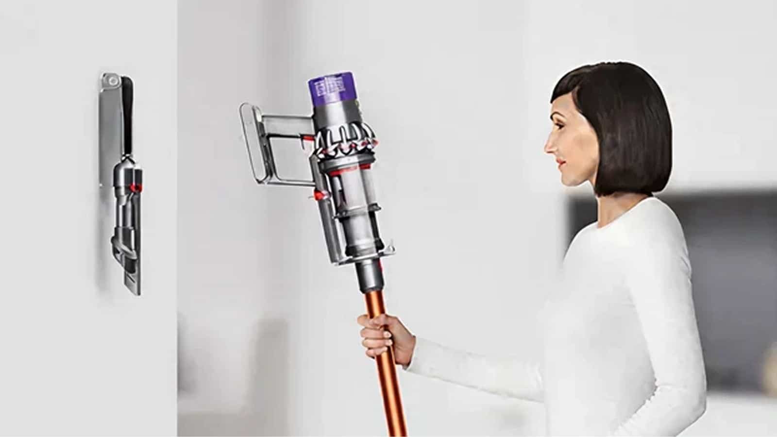 Femme tenant un aspirateur balai Dyson Cyclone V10 à tube cuivré près de sa station murale