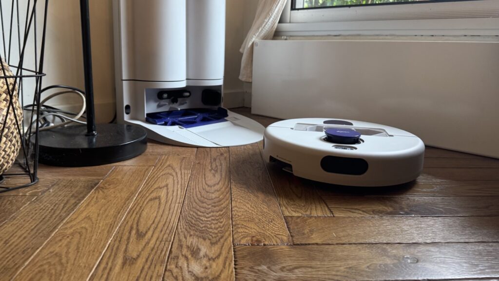 Le robot aspirateur laveur Dyson R2 Nurovi Wash+Dry quitte sa station blanche sur un parquet, dans un salon