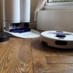 Le robot aspirateur laveur Dyson R2 Nurovi Wash+Dry quitte sa station blanche sur un parquet, dans un salon