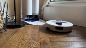 Le robot aspirateur laveur Dyson R2 Nurovi Wash+Dry quitte sa station blanche sur un parquet, dans un salon