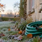 Robinet extérieur en laiton sur un mur de pierre, tuyau d’arrosage enroulé au pied et herbe givrée un matin d’automne