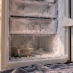 Congélateur armoire ouvert dans une cuisine, parois et bord des tiroirs couverts d’une épaisse couche de givre blanc