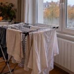 Un étendoir chargé de linge humide devant une fenêtre embuée, dans un salon chauffé